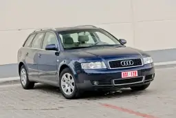 Ciemnoniebieskie Audi A4 B6 Avant na parkingu. Widać przednie reflektory i grill z logo Audi.