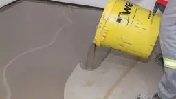 Wylewanie samopoziomującej masy z żółtego wiadra na podłogę.