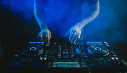 DJ grający na konsoli w niebieskiej chmurze dymu.