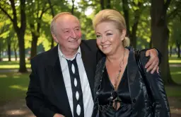 Uśmiechnięta para w eleganckich strojach na tle parku.