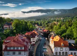 Widok na urokliwe miasteczko Szklarska Poręba z czerwonymi dachami, otoczone bujną zielenią i mglistymi Karkonoszami.