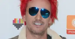 Michał Wiśniewski w okularach przeciwsłonecznych i z czerwonymi włosami. Choć nie widać całego ciała, jego postawa sugeruje, że ile wzrostu ma Michał Wiśniewski, nie jest kluczowe dla jego charyzmy.