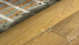 Układanie podłogi z ogrzewaniem podłogowym w salonie 30 m2. Widać pętle grzewcze i nowe deski.