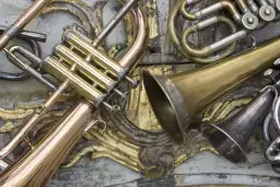 Złote i srebrne instrumenty dęte, jak trąbka i róg, leżą na ozdobnym tle.