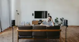 Kobieta siedzi na kanapie w salonie z głośnikami kina domowego rozmieszczonymi wokół.