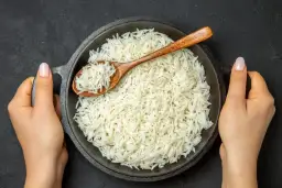 Sypki ryż basmati w misce, nabierany drewnianą łyżką, trzymany przez dwie dłonie.