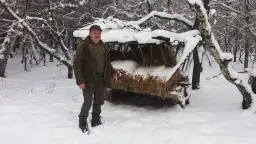 Mężczyzna w zimowym lesie przy paśniku z sianem.