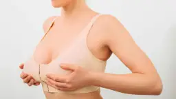 Kobieta w cielistym biustonoszu z zapięciem z przodu, ręce na piersiach.