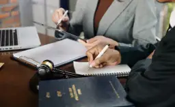 Prawnicy analizują dokumenty, dyskutując o potencjalnej dewastacji. Na stole młotek sędziowski i laptop.