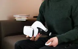 Osoba w zielonym swetrze trzyma białe okulary VR i kontroler. Dowiedz się, jak podłączyć okulary VR do komputera.