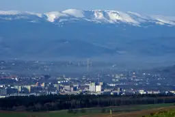 Widok na miasto u podnóża ośnieżonych gór. Trudno oszacować, ile jelenia góra ma mieszkańców, ale miasto jest spore.