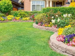 Piękne obrzeża ogrodowe pomysły: bujna zieleń trawnika, kolorowe kwiaty i kamienne murki tworzą malowniczy krajobraz.