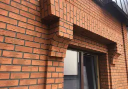 Fragment elewacji z cegły klinkierowej z ozdobnym gzymsem nad oknem.