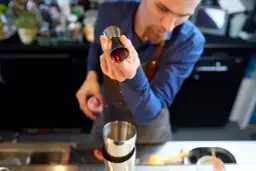 Barman przelewa czerwony płyn z jiggera do shakera.