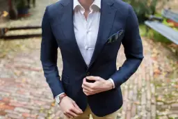 Mężczyzna w granatowej marynarce, białej koszuli i z poszetką w kratę.