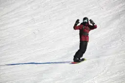 Snowboardzista w czerwonej kurtce z rękami w górze na ośnieżonym stoku.