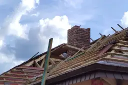 Budowa dachu z ceglanym kominem. Zastanawiasz się, czy komin można ocieplić styropianem? Na zdjęciu widać konstrukcję dachu i komin.