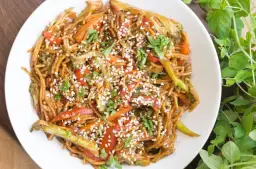 Pyszny azjatycki makaron z sosem sojowym, brokułami, papryką i marchewką, posypany sezamem.