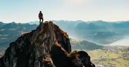 Wspinacz na szczycie skalistego wzniesienia, podziwia letnie krajobrazy Alp.