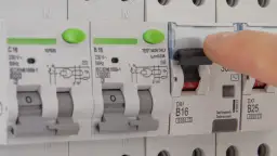 Dłoń naciska dźwignię wyłącznika, który jest częścią instalacji elektrycznej. Czy różnicówka jest obowiązkowa? To pytanie o bezpieczeństwo.