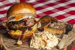 Burger z jajkiem sadzonym, bekonem, frytkami i surówką colesław na drewnianej desce.
