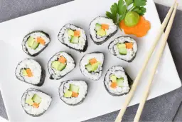 Talerz z sushi z awokado, ogórkiem i marchewką, pałeczki i wasabi.