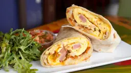 Pyszny omlet z tortillą, jajecznica, szynka i ziemniaki zawinięte w placek. Obok sałatka i salsa.