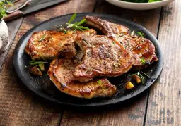 Grillowane kotlety z baraniny z ziołami na czarnym talerzu.