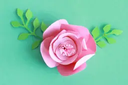 Kwiaty z papieru 3d jak zrobić? Różowa róża z zielonymi listkami, idealna do dekoracji.
