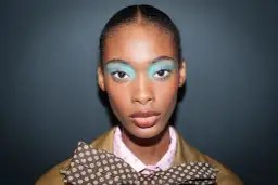 Modelka z turkusowymi cieniami do powiek i kokardą. Modne makijaże na wybiegu.