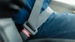 Osoba zapina środkowy pas bezpieczeństwa w samochodzie. Pasek jest wpięty w klamrę.