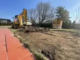 Koparka przygotowuje teren pod trawnik. Widać kopiec ziemi i wykopane rowy. Ile ziemi pod trawnik na m2?