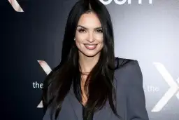 Uśmiechnięta Klaudia El Dursi, której wiek jest tajemnicą, pozuje na tle czarnej ściany z logo.