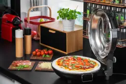 Gotowa pizza na kamieniu w otwartym piecyku, obok składniki: pomidorki, rukola, szynka, ser.
