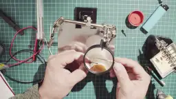 Precyzyjne lutowanie przewodów 230v pod lupą. W tle lutownica i zapalniczka.