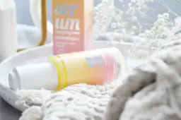 Butelka serum rozświetlającego OnlyBio na białej tacy, obok pudełka i białych kwiatów.