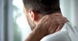 Mężczyzna masuje kark, czując ból. Czy to znak, że sennik diagnoza rak może mieć sens?