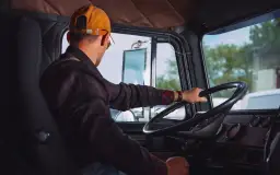 Kierowca w czapce i koszuli w kratę trzyma kierownicę. Pamiętaj o regularnym szkoleniu BHP kierowcy co ile.