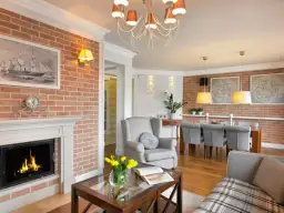 Przytulny kominek w salonie z palącym się ogniem, obok wygodny fotel i stolik kawowy.