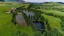 Widok z lotu ptaka na stawy rybne otoczone zielenią, z domami w tle.