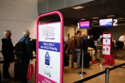 Tablica Wizzair z zasadami bagażu podręcznego, w tle kolejka pasażerów do odprawy.