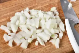 Posiekana cebula na desce do krojenia obok noża.