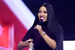 Nicki Minaj z mikrofonem, w ciemnej sukience, z długimi czarnymi włosami i biżuterią.