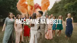 Para młoda całuje się na tle weselnych gości, którzy trzymają race dymne w kolorach tęczy.