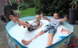 Dwóch chłopców bawi się w basenie wypełnionym pianą, jeden pokazuje kciuk w górę.