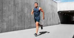 Mężczyzna w stroju sportowym biegnie przy betonowej ścianie.