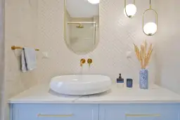 Nowoczesna łazienka z białą umywalką, złotymi bateriami i lustrem na tle kafli w jodełkę.