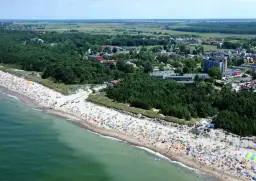Dąbki: warto jechać! Tłumy ludzi na plaży, zielone lasy i budynki kurortu. Idealne miejsce na wakacje.