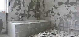 Łazienka w trakcie remontu, z odsłoniętymi ścianami i gruzem.