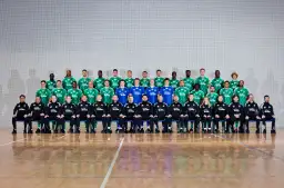 Radomiak Radom zawodnicy w zielonych strojach pozują do wspólnego zdjęcia. W tle siatka, na pierwszym planie parkiet.